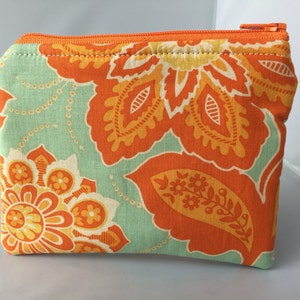 May include: A small orange and green zippered pouch with a floral pattern. The pouch is made of fabric and has a zipper closure.