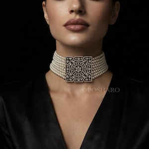 Puede incluir: Un collar de gargantilla de perlas con una pieza central cuadrada y ornamentada. La pieza central es oscura con un diseño detallado y está incrustada con pequeñas piedras brillantes. El collar tiene múltiples hilos de perlas.