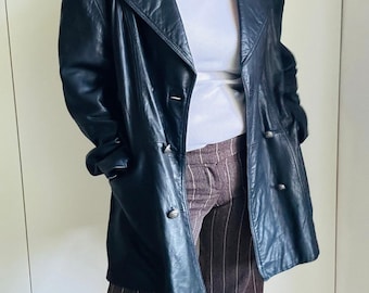 May include: A black leather jacket with a double-breasted design. The jacket has a notched collar, two front pockets, and silver-tone buttons. The model is wearing a white t-shirt and brown striped pants. The jacket appears to be vintage.