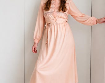 Könnte beinhalten: Ein vintage-farbenes Pfirsichkleid mit langen Ärmeln und einem knielangen Rock. Das Kleid hat einen hohen Ausschnitt mit Spitzendetails und eine Bindetaille. Ein passender Barett vervollständigt das Outfit.
