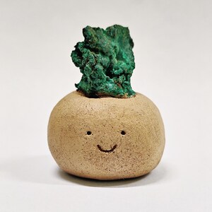 May include: A small, brown ceramic planter with a smiling face and a green malachite stone on top.