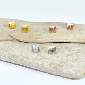 Peut inclure: Cinq paires de boucles d'oreilles carrées dans différentes finitions métalliques. Les boucles d'oreilles sont présentées sur un morceau de bois flotté.