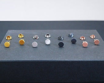 May include: A display of 12 small round stud earrings in various metallic finishes, including gold, silver, black, and rose gold.