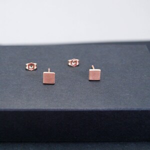 May include: A pair of rose gold square stud earrings. The earrings are small and simple, and they would make a great everyday accessory.