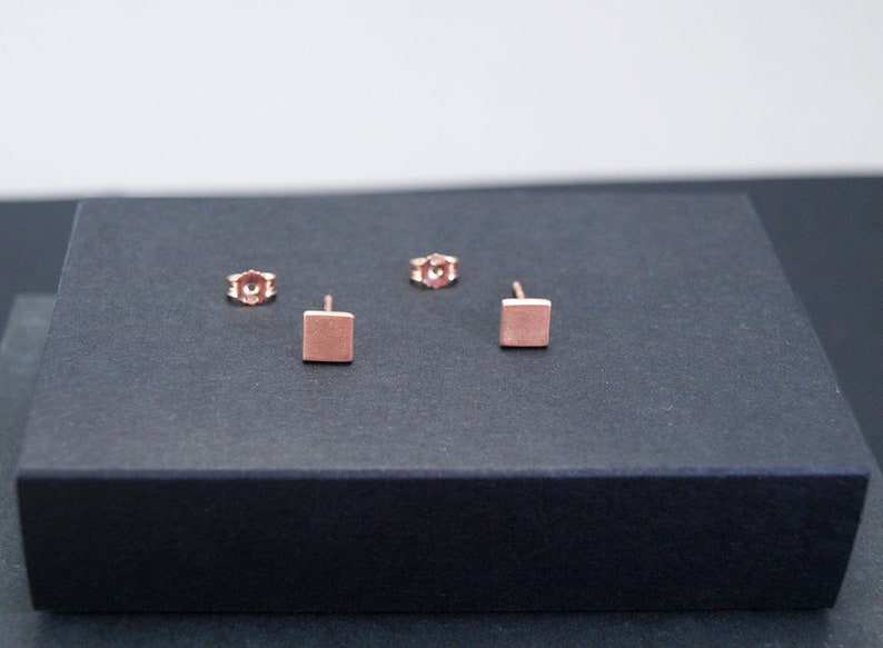 May include: A pair of rose gold square stud earrings. The earrings are small and simple, and they would make a great everyday accessory.