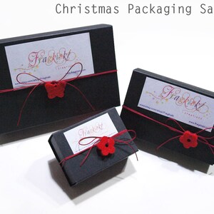 May include: Three black gift boxes with red ribbon and red felt flower embellishments. The boxes are labeled with the text "Fragkiskl Creatives" and a website address.