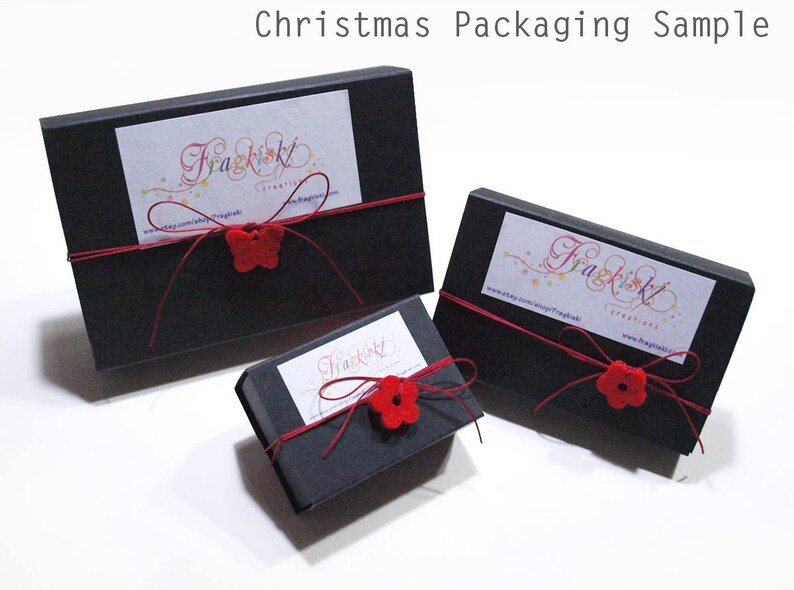 May include: Three black gift boxes with red ribbon and red felt flower embellishments. The boxes are labeled with the text "Fragkiskl Creatives" and a website address.