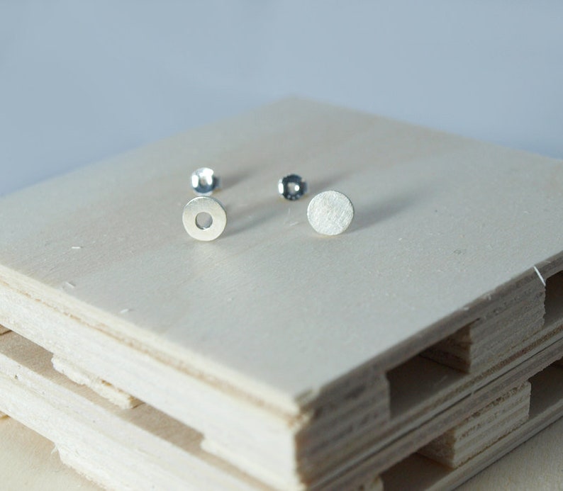 May include: A pair of silver earrings, one with a solid round disc and the other with a round disc with a hole in the center.