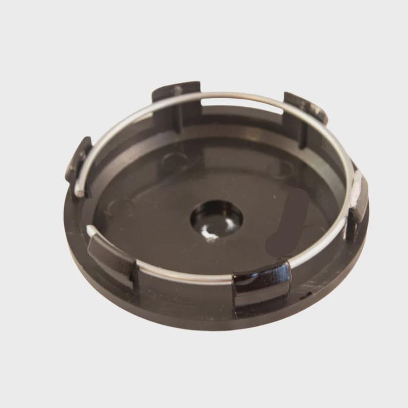 K&ouml;nnte beinhalten: Eine kreisf&ouml;rmige Radnabenabdeckung aus schwarzem Kunststoff mit einem silberfarbenen Metallspannring, der am inneren Rand befestigt ist. Das Bauteil verf&uuml;gt &uuml;ber mehrere geformte Kunststoffclips am Rand f&uuml;r eine einfache Montage.