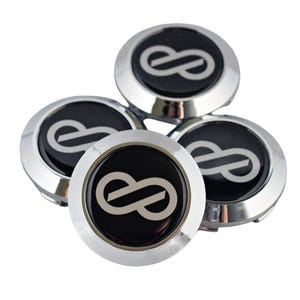 K&ouml;nnte beinhalten: Ein Set aus vier runden Radnabendeckeln mit einem &auml;u&szlig;eren Ring aus poliertem Chrom und einem schwarzen Inlay. Jeder Deckel zeigt ein silbernes Unendlichkeitssymbol, das mittig auf der schwarzen Oberfl&auml;che platziert ist, mit glatter Optik.
