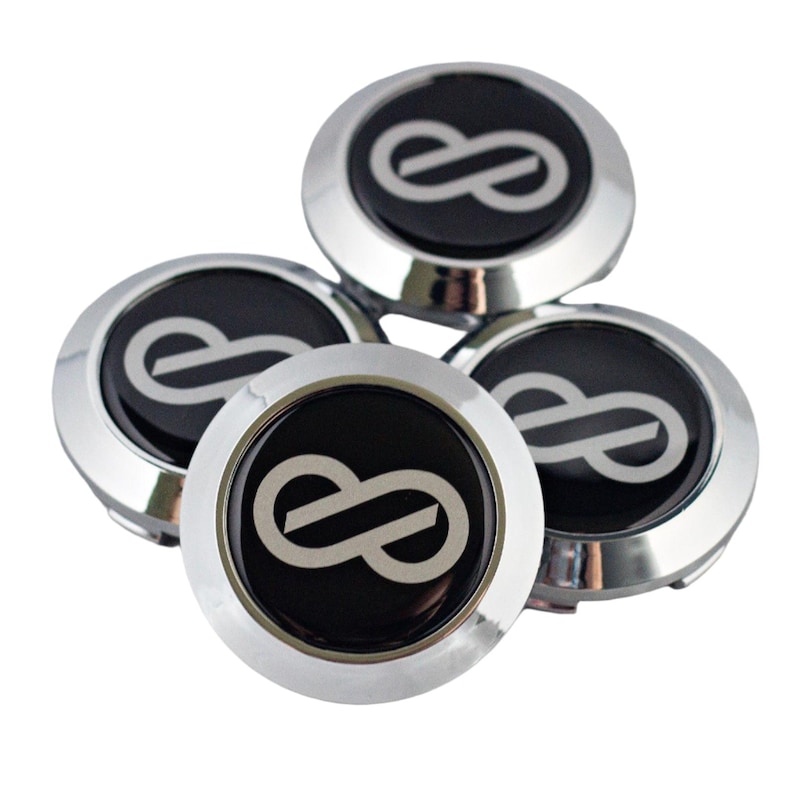 K&ouml;nnte beinhalten: Ein Set aus vier runden Radnabendeckeln mit einem &auml;u&szlig;eren Ring aus poliertem Chrom und einem schwarzen Inlay. Jeder Deckel zeigt ein silbernes Unendlichkeitssymbol, das mittig auf der schwarzen Oberfl&auml;che platziert ist, mit glatter Optik.