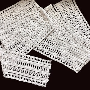 May include: White crocheted lace trim with a delicate pattern. The lace is folded and arranged in a decorative way.