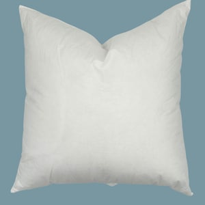 May include: A square, white pillow with a soft, textured appearance. The pillow is centered against a light blue background. The pillow has a pointed top and bottom. The brand name "JILLIEN HARBOR" is printed at the bottom.