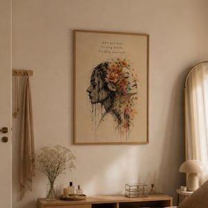 May include: A framed wall art print featuring a dual-profile illustration of a person. One side is rendered in dark, dripping ink, while the other is adorned with vibrant, colorful floral details. The text reads, who are you losing while finding yourself.