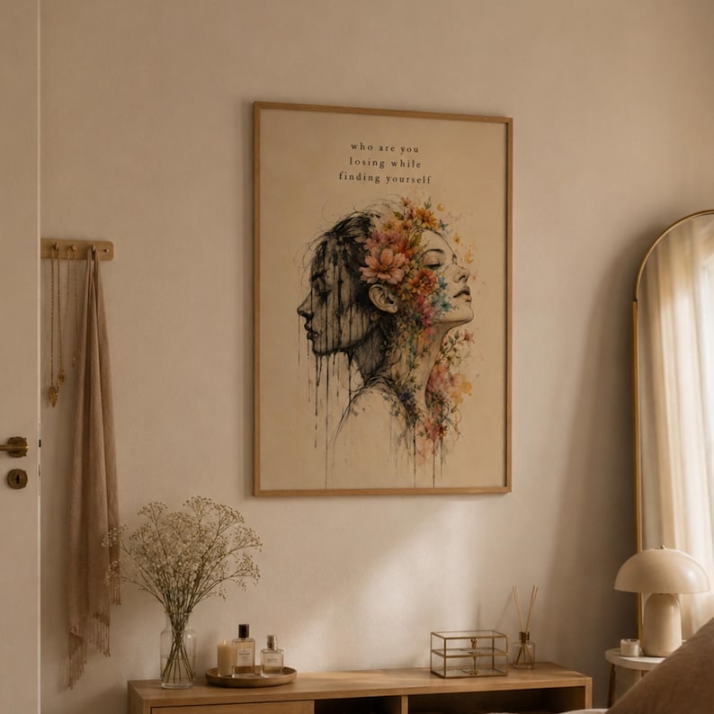 May include: A framed wall art print featuring a dual-profile illustration of a person. One side is rendered in dark, dripping ink, while the other is adorned with vibrant, colorful floral details. The text reads, who are you losing while finding yourself.