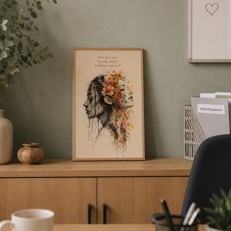 May include: A rectangular framed wall art print featuring a dual-profile illustration of a person with watercolor-style floral accents in orange, yellow, and blue. The text "who are you losing while finding yourself" is printed above the illustration.