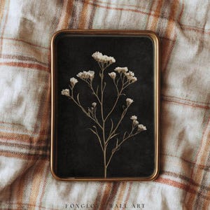 May include: A framed botanical print featuring a sprig of white flowers against a dark background. The rectangular frame has a gold finish. The text "FONGLOW WALL ART" is visible at the bottom of the frame.