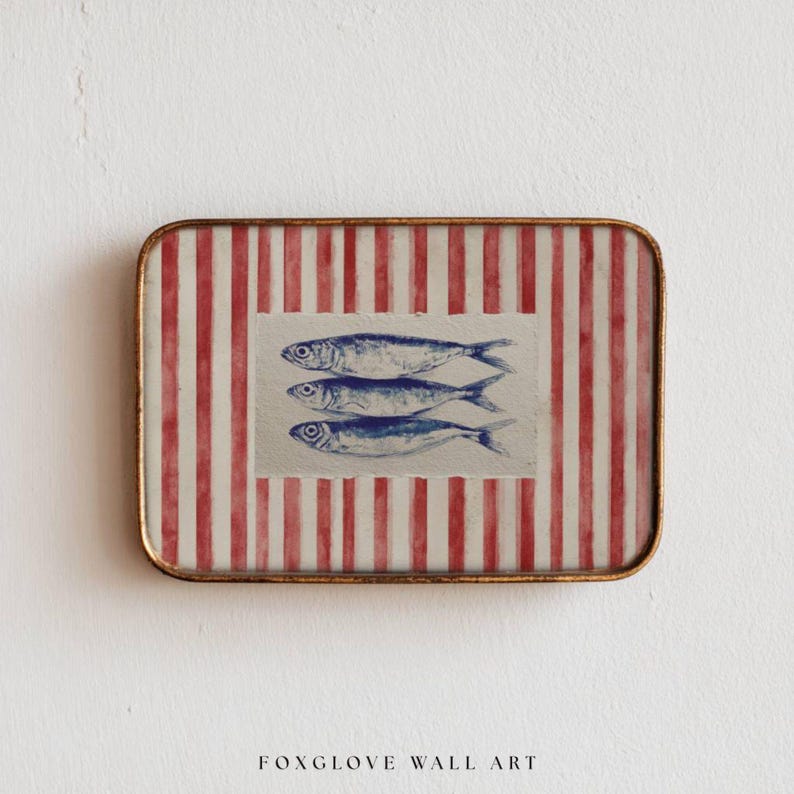 May include: Rectangular wall art featuring three blue fish illustrations on a cream background, set against a red and white striped pattern. The artwork is framed with a gold-colored metal edge. The text "FOXGLOVE WALL ART" is at the bottom.