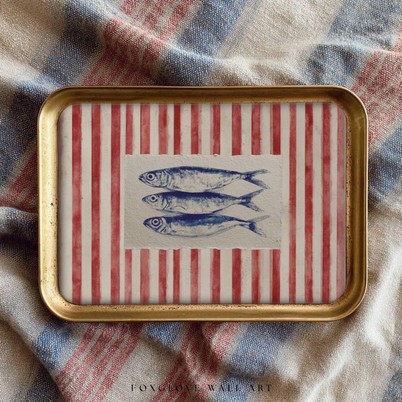 May include: A rectangular serving tray with a gold rim. The tray's interior features a red and white striped pattern with a central rectangular image of three blue fish. The background is a textured fabric.