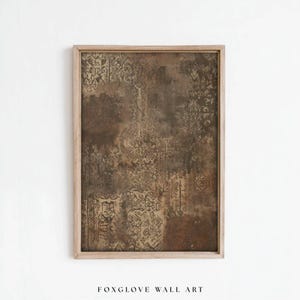 May include: A rectangular wall art piece in a light wood frame featuring a dark brown and tan abstract pattern with layered, weathered textures and intricate, faded geometric motifs that resemble aged fabric or distressed vintage wallpaper.