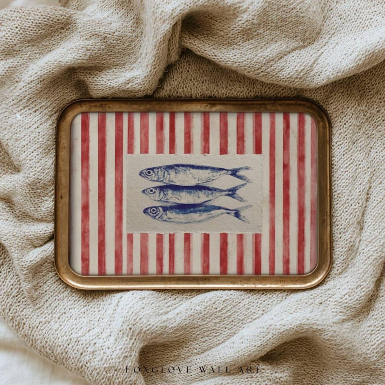 May include: A rectangular tray with a gold-colored frame. The tray's interior features a red and white striped background with a rectangular section in the center. Three blue fish are depicted on the rectangular section. The text "FOXGLOVE WALL ART" is at the bottom.