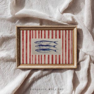 May include: Framed wall art featuring three blue fish illustrations on a white background, set against a red and white striped pattern. The artwork is enclosed in a gold-colored frame. The text "FOXGLOVE WALL ART" is at the bottom.