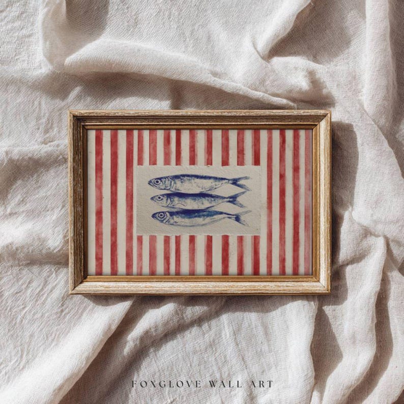 May include: Framed wall art featuring three blue fish illustrations on a white background, set against a red and white striped pattern. The artwork is enclosed in a gold-colored frame. The text "FOXGLOVE WALL ART" is at the bottom.