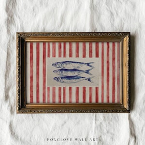 May include: Framed wall art featuring three blue fish illustrations on a textured paper. The background has red and white vertical stripes. The frame is gold-colored with ornate detailing. The text "FOXGLOVE WALL ART" is at the bottom.