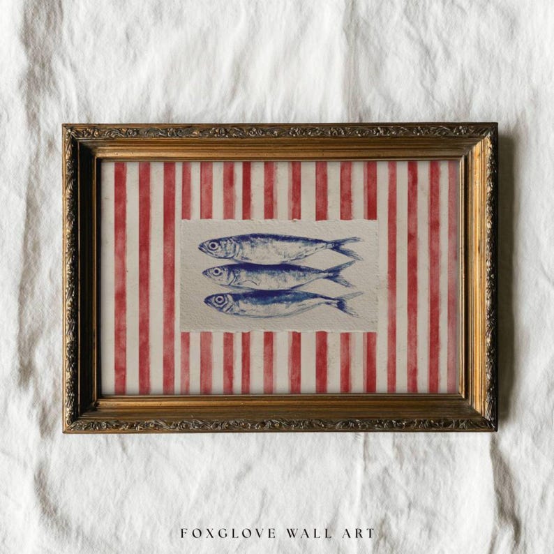 May include: Framed wall art featuring three blue fish illustrations on a textured paper. The background has red and white vertical stripes. The frame is gold-colored with ornate detailing. The text "FOXGLOVE WALL ART" is at the bottom.