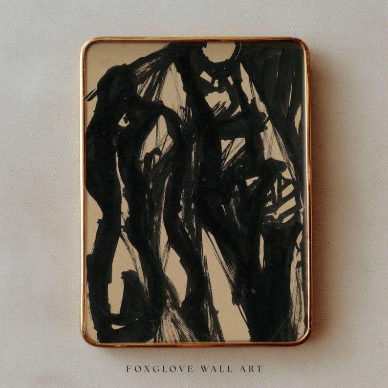 May include: Abstract art print in a rectangular gold frame. The artwork features bold black brushstrokes on a beige background. The text "FOXGLOVE WALL ART" is printed at the bottom of the frame.