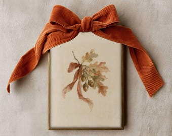 Puede incluir: Una impresión rectangular enmarcada que presenta una ilustración en acuarela de hojas de roble y bellotas atadas con una cinta. Un gran lazo de tela texturizada de color naranja quemado está sujeto a la parte superior del marco dorado. El texto FOXGLOVE WALL ART es visible.