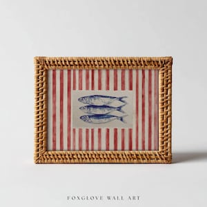 May include: A framed wall art print featuring three blue fish illustrations on a textured background. The background has red and white vertical stripes. The frame is made of woven wicker. The text "FOXGLOVE WALL ART" is at the bottom.