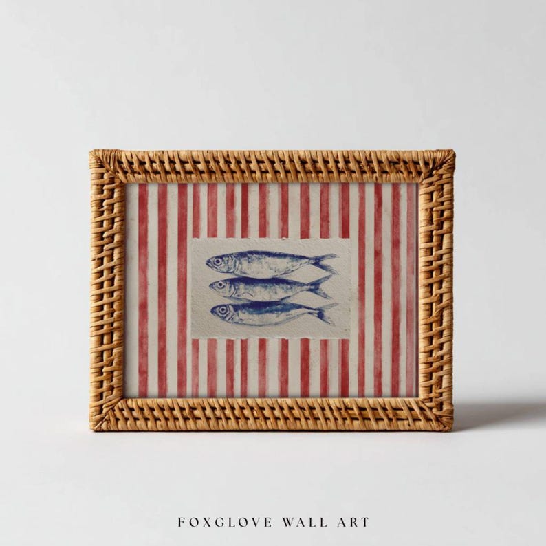May include: A framed wall art print featuring three blue fish illustrations on a textured background. The background has red and white vertical stripes. The frame is made of woven wicker. The text "FOXGLOVE WALL ART" is at the bottom.