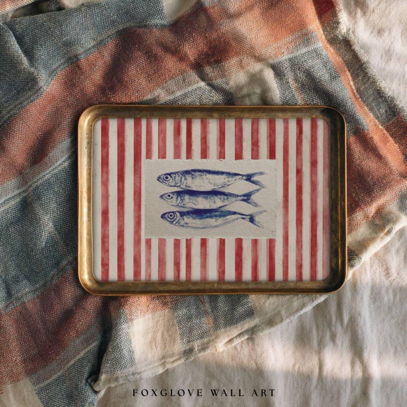 May include: A rectangular tray with a gold-colored frame. The tray's interior features a red and white striped pattern with three blue fish illustrations. The tray is placed on a patterned fabric with red, white, and blue stripes. Text at the bottom reads "FOXGLOVE WALL ART."