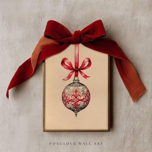 May include: A framed print featuring a Christmas ornament design with red and white detailing, suspended by a red ribbon and bow. The frame is gold-toned, and the artwork is set against a neutral background. The text "FOXGLOVE WALL ART" is at the bottom.
