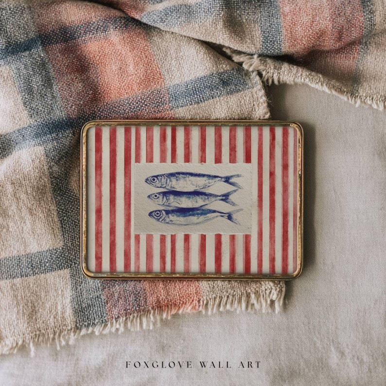 May include: Rectangular wall art with a gold frame. The artwork features a red and white striped background with three blue fish illustrations. The text "FOXGLOVE WALL ART" is at the bottom. The art is set on a textured fabric.