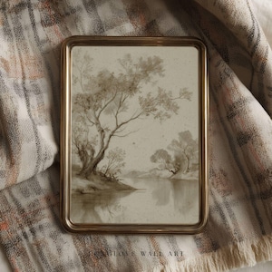 May include: A sepia-toned landscape art print in a gold frame. The artwork depicts trees and their reflection in a body of water. The frame is rectangular with rounded corners. The print is displayed on a patterned fabric.