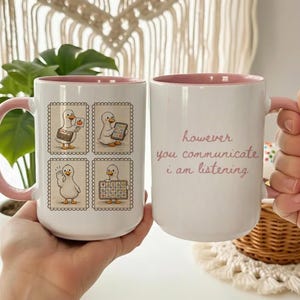 Puede incluir: Taza de cerámica blanca con interior y asa rosas. La taza presenta un pato de dibujos animados en cuatro poses diferentes, y el texto "however you communicate i am listening".