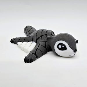 Könnte beinhalten: Eine 3D-gedruckte Eichhörnchenfigur in Grau und Weiß, die auf dem Bauch liegt. Das Eichhörnchen hat einen detaillierten, strukturierten Körper und ein weißes Gesicht mit schwarzen Augen. Ein einzigartiges Dekorationsstück.