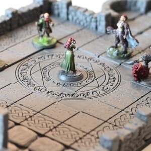 Op de afbeelding: Een grijze miniatuur kerker terrein set met stenen muren, bogen en een cirkelvormig ontwerp. Verschillende miniatuurfiguren zijn op het terrein geplaatst, wat wijst op een tabletop rollenspel omgeving. De set is ontworpen voor fantasy games.