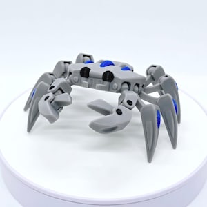 May include: A gray, mechanical crab toy with articulated legs and claws. The crab has blue accents on its body and legs, and black details on its head. The toy is designed with a futuristic aesthetic.