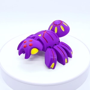 Pode incluir: Um inseto de brinquedo articulado roxo com detalhes amarelos e vermelhos. O brinquedo tem um corpo segmentado, várias pernas e uma cabeça arredondada. O design apresenta formas geométricas e provavelmente é impresso em 3D.