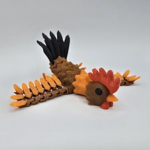 May include: A colorful, articulated chicken figurine. The body is brown and orange, with a black tail. The head features a red comb and wattle, a brown face, and an orange beak. The wings are made of orange and brown pieces.