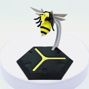 Pode incluir: Modelo impresso em 3D de uma abelha, com corpo listrado amarelo e preto, pernas pretas e asas cinzentas. A abelha é montada em um suporte curvo cinza, fixado a uma base hexagonal preta com detalhes amarelos.
