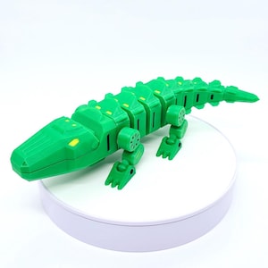 May include: A bright green articulated crocodile toy with yellow accents. The toy is made of connected segments, allowing for flexible movement. The crocodile is posed on a white surface, showcasing its detailed design and playful nature.