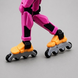 May include: Close-up of a pair of roller skates with orange and black accents. The skates have gray wheels and are attached to a pink leg. The image is set against a gray background.