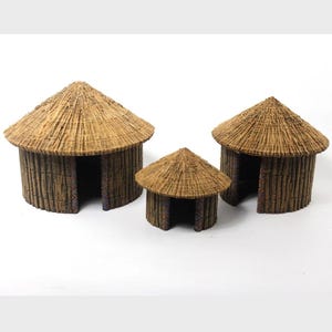 May include: Three miniature huts with thatched roofs and textured brown walls. The huts vary in size, with the largest on the left and the smallest in the center. The huts have open doorways and decorative patterns around the openings.