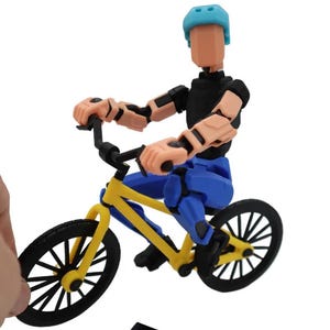 May include: A blue and black articulated action figure riding a yellow BMX bike with black wheels. The figure is wearing a blue helmet.
