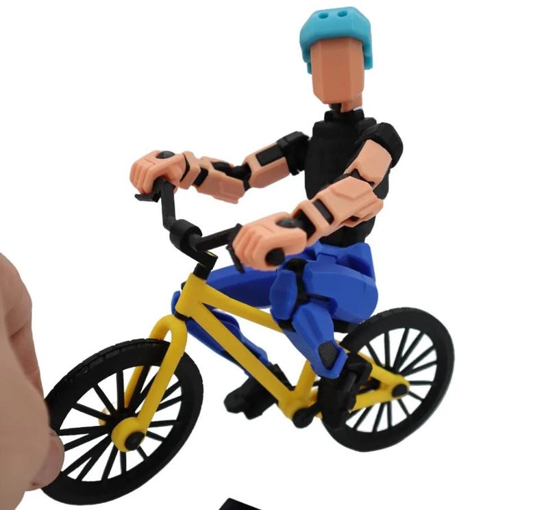 May include: A blue and black articulated action figure riding a yellow BMX bike with black wheels. The figure is wearing a blue helmet.