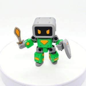 May include: A green and grey robot figure holding a sword and shield. The robot has a square head with a screen-like face and orange eyes. The sword and shield are grey and orange.